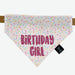Pink sprinkle motif bandana with the words "Birthday girl" in dark pink. The dog bandana is held up on a tan leather collar and placed on a white background.