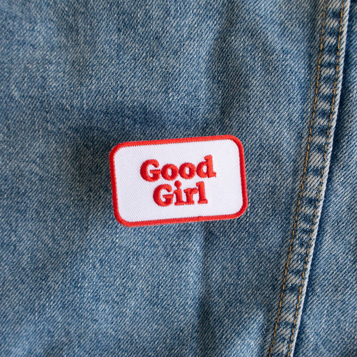 Scouts Honour "Good Girl" iron-on badge with red text and a white background, laid out on a denim backdrop