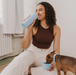Dog and human drinking from  the Sky Blue "Dog & Me" Reusable Insulated Bottle. The bottle features a brushed chrome top with handle.