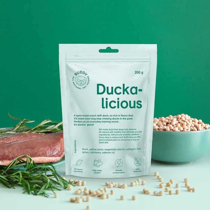 The image shows a bag of Buddy's Duckalicious treats. Next to it some yellow peas and a duck breast are pictured.
